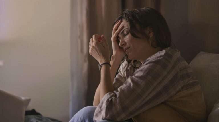 A distressed woman sitting in dim lighting, holding her head in pain, showing Can Hypnosis Help PTSD? How Trauma-Focused Hypnotherapy Creates Lasting Change.