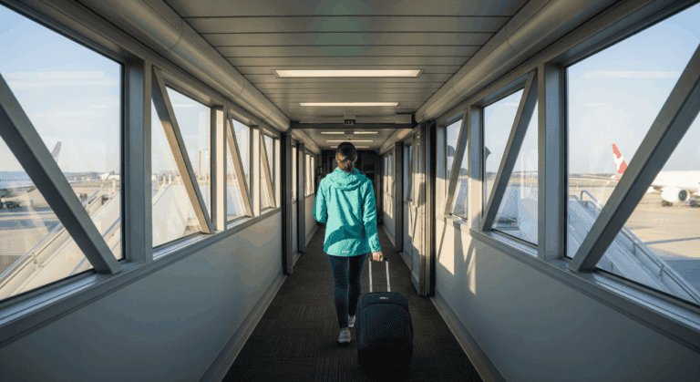 Solo traveler walking with luggage toward an airplane jet bridge.