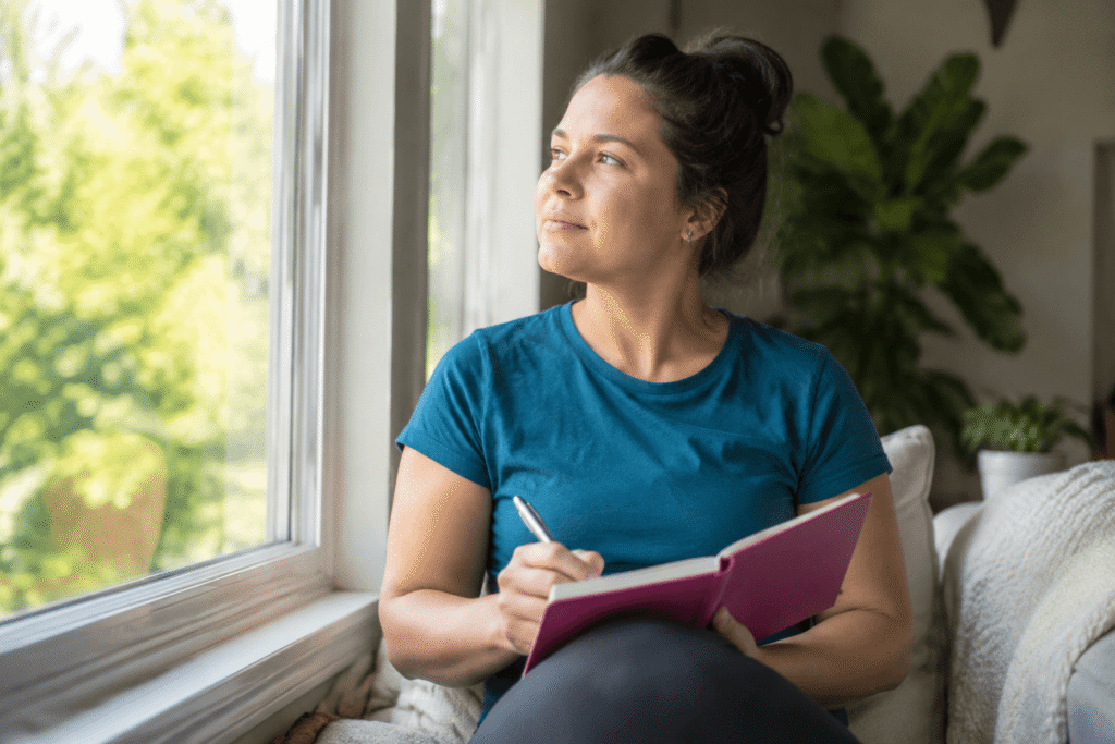 Woman journaling by window, representing hypnosis for changing self-sabotaging patterns